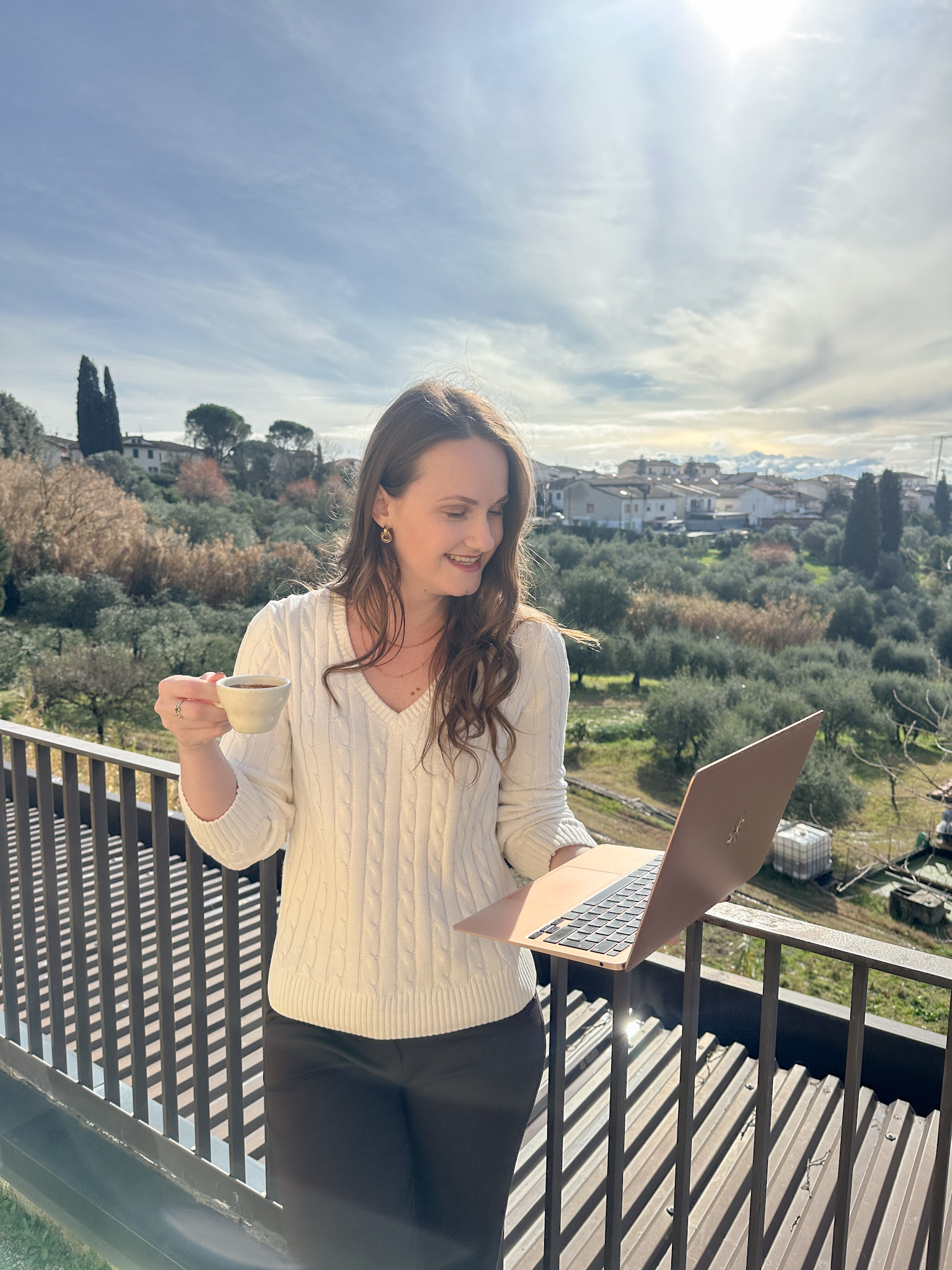 Valeria working outdoors with coffee and laptop in Tuscany